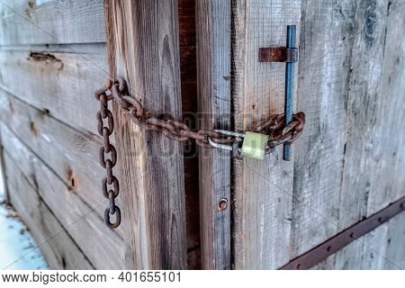 Closed Wood Door Of Outdoor Bathrooom With Rusty Chain And Long Shackle Padlock