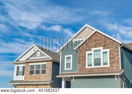 Gabled Homes With Stone Brick And Wooden Siding On Walls Against Cloudy Blue Sky