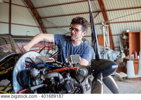 A Man Cheking Avia Oil In Small Aircraft. Airplane In Hangar. Repaiper Holding Instruments Near The 