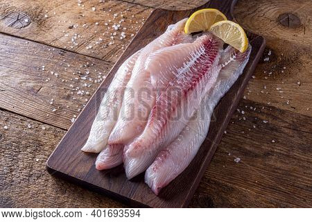 Fresh Haddock Fillets On A Rustic Table Top With Lemon Wedges.