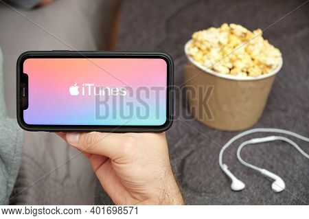 Close Up Mans Hand Holding A Mobile Phone With Itunes Logo With Apple Earphones And Popcorn Box Next