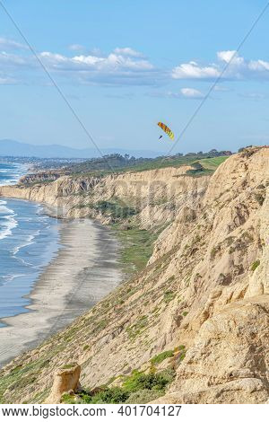 Rocky Mountain Bordering The Shoreline Of Ocean Aith Parachuters And Blue Sky