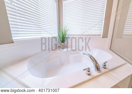 Built In Bathtub Inside A Bathroom With Indoor Plant And Two Windows With Blinds