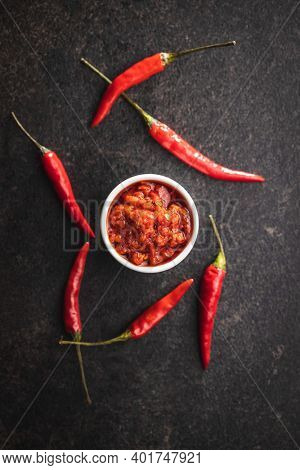 Red hot chili paste and chili pepper in bowl on black table. Top view.