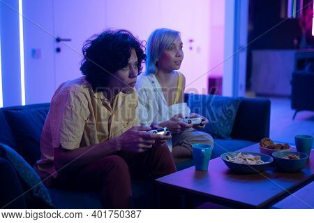 Couple Of Young Adults Playing Video Games At Home. Emotional Diverse Gamers Holding Joysticks And C