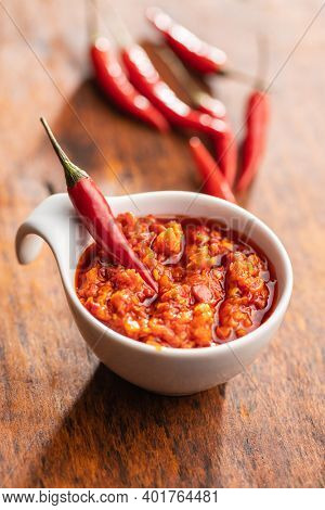 Red hot chili paste and chili pepper in bowl on wooden table.