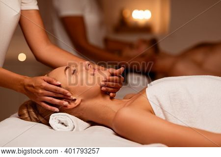Woman Receiving Face Massage During Relaxing Couples Therapy Enjoying Treatment Lying On Bed In Luxu
