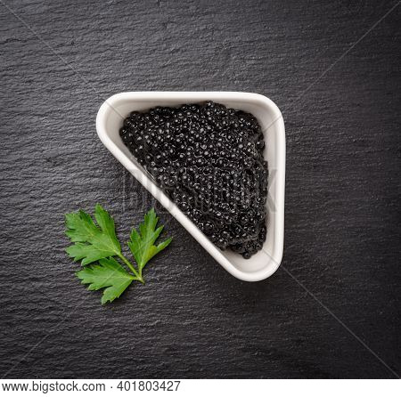 Black Grainy Caviar Of Paddlefish Fish In A White Ceramic Bowl, Black Background, Top View