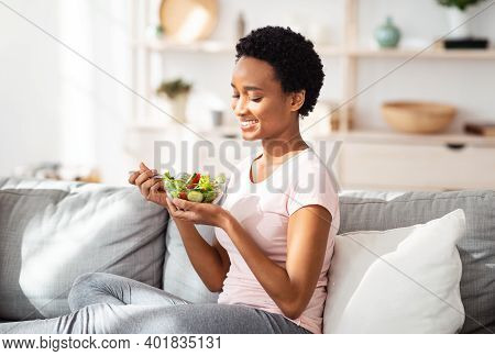 Balanced Nutrition Concept. Lovely Black Lady Eating Delicious Vegetable Salad On Cozy Couch At Home