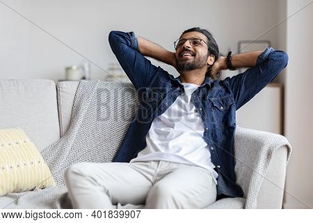 Relaxed Smiling Arab Guy Leaning Back On Couch At Home, Relaxing After Successful Day, Positive Youn