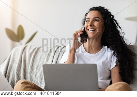 Cheerful Young Woman Freelancer Talking On Mobile Phone And Using Laptop, Working From Home During I
