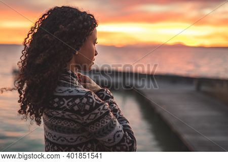 Young African American Woman Is Standing On The Promenade At The Lake, Looking Thoughtfully Towards 