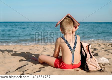 Happy Young Boy Reading A Book On A Sunny Dayl. Boy Sitting With His Back At The Beach. Last Day Of 