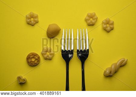 Two Forks With Some Types Of Colored Pasta On A Yellow Surface