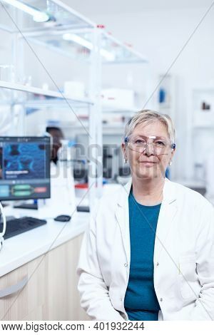 Smiling Senior Chemist Wearing Protective Glasses With Test Tubes Behind. Elderly Scientist Wearing 
