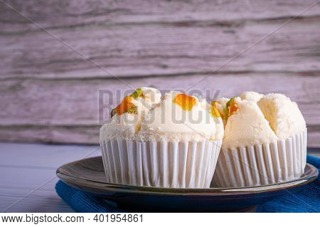 Side View Of Thai Steamed Cupcakes Topped With Dry Fruit On A Plate On A Blue Cloth With A Wooden Ba