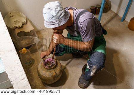 Man Making Pickles In A Ceramic Vasel Using An Old Recipy. He Enriches The Contents Of The Vessel Wi