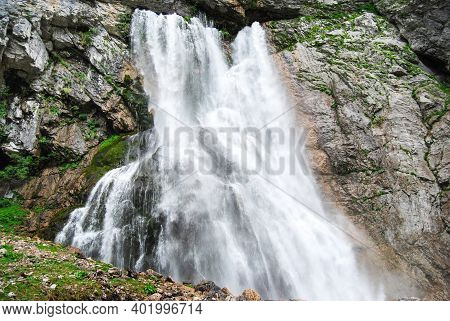 Mountain Waterfall. A Powerful Mountain River Bursts Out Of A Mountain Crevice And Falls Like A Wate