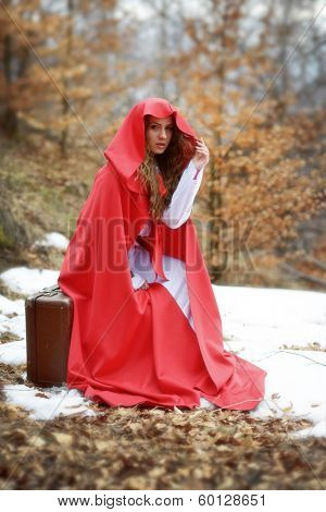 beautiful woman with red cloak sitting on suitcase