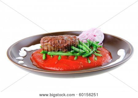 pork medallion served on tomato sauce with green peas on dark plate isolated on white background