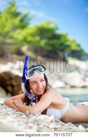 Pretty, young woman on a beach during her summer vacation with snorkel lying on beach with snorkeling mask and fins smiling happy enjoying the sun on a sunny summer day.