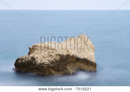 Rock in ruhiger See mit blauer Himmel