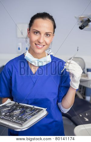 Smiling dentist holding tray and angle mirror in dental clinic