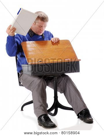 A mature adult student pulling supplies out of the retro child's school desk in which he's sitting.  On a white background.