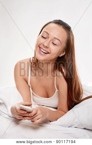 Radiant woman with phone lying on bed