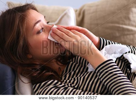 Portrait of a sick woman blowing her nose while sitting on the sofa