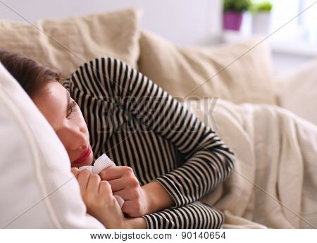 Portrait of a sick woman blowing her nose while sitting on the sofa