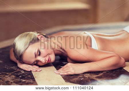people, beauty, spa, healthy lifestyle and relaxation concept - beautiful young woman lying on hammam table in turkish bath