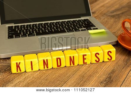 Kindness written on a wooden cube in a office desk