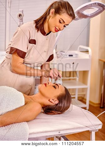 Lying young woman receiving electroporation  facial therapy at beauty salon. 
