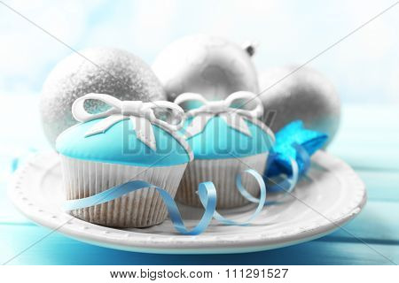 Tasty cupcakes with bow and Christmas toys on color wooden background