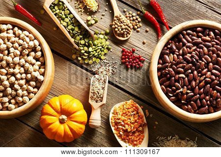 Bowls and spoons of various legumes on wooden background