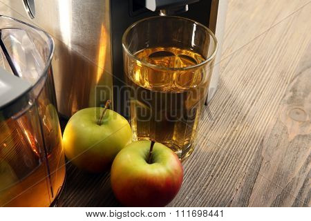 Stainless juice extractor with apples and glass of juice on wooden background, close up