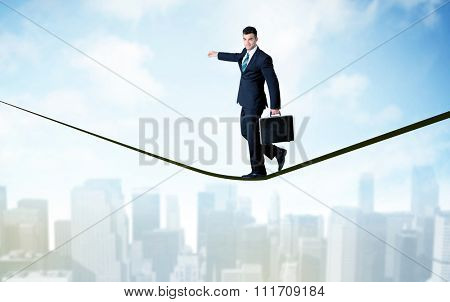City scape, tall buildings and clouds on clear blue sky with business person balancing on black rope concept