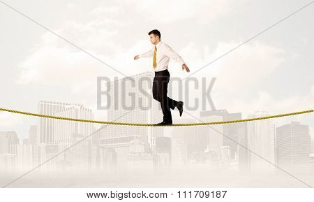A young elegant businessman walking on tight golden rope in front of city buildings landscape background concept