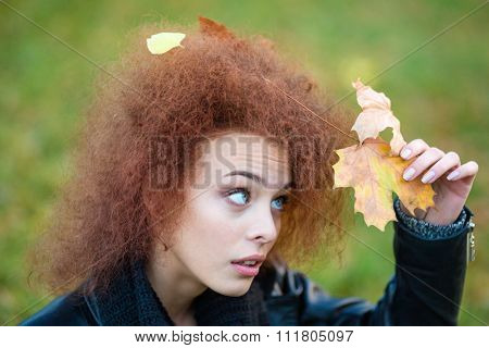 Portrait of a funny woman looking up on leaves in her curly hair outdoors