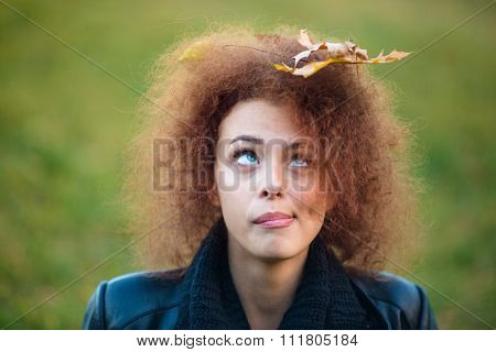 Portrait of a funny woman looking up on leave in her curly hair outdoors