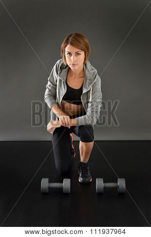 Fitness girl knelt on floor lifting dumbbells, isolated 