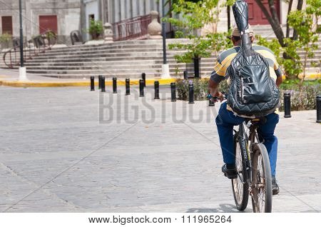 Man with guitar backback and hat on bicycle bike in the street of Granada