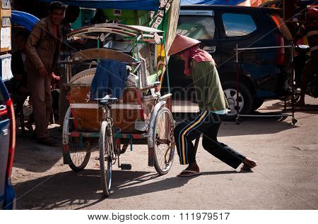 Man with hat Pumping Air Into The Wheel of his tricycle
