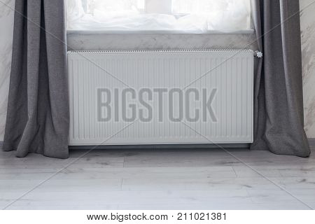 Part of a bright room with heating convector radiator installed under the window.