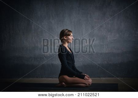 Beautiful sporty fit yogini woman practices yoga asana Vajrasana - diamond pose in the dark hall.