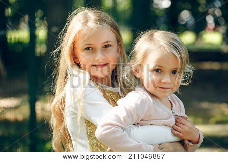 Gentle love of two sisters. Girls embrace each other with healthy smiles and positive minds. Elder sister holds younger on her hands.