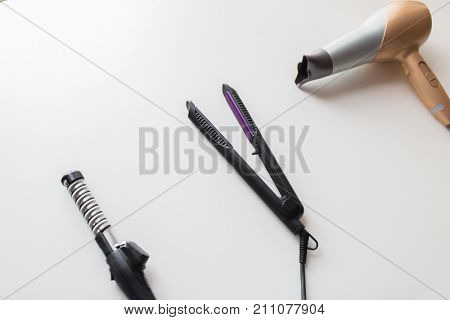 hair tools, beauty and hairdressing concept - hairdryer, hot styler and curling iron or tongs on white background