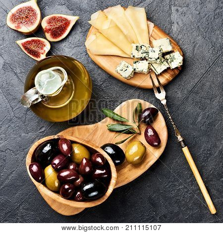 Italian snacks food with Cheese, Olives, Oil and Figs on black concrete background with copy space. Top view.