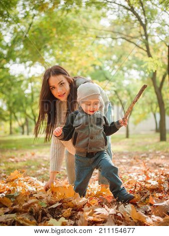 Mom plays with his son in the autumn in the park against the backdrop of fallen leaves